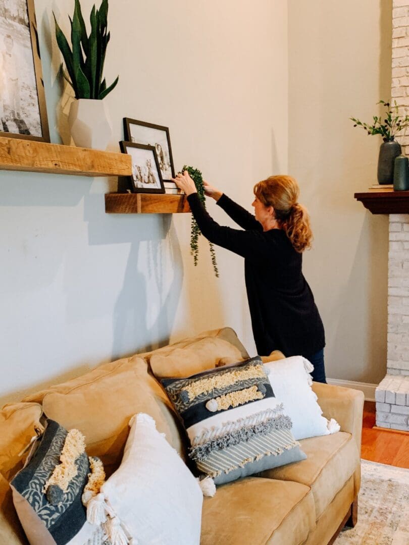 A woman hanging pictures on the wall above her couch.