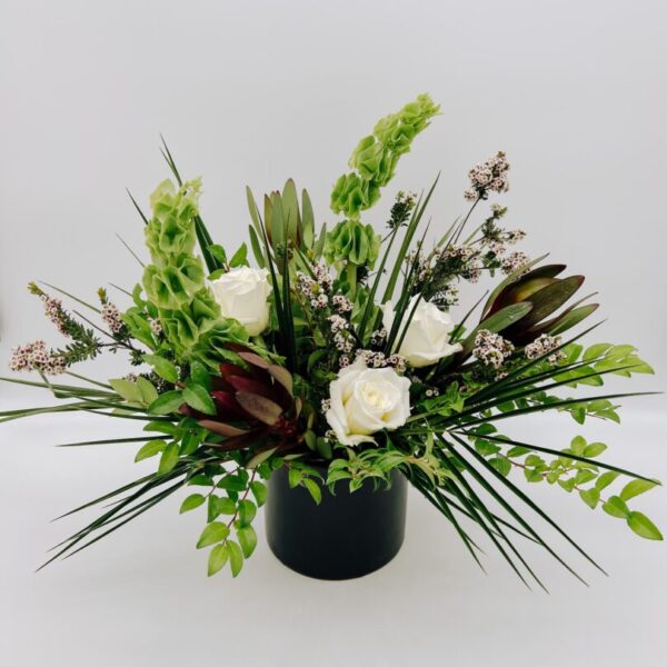 A black vase with white flowers and green plants.